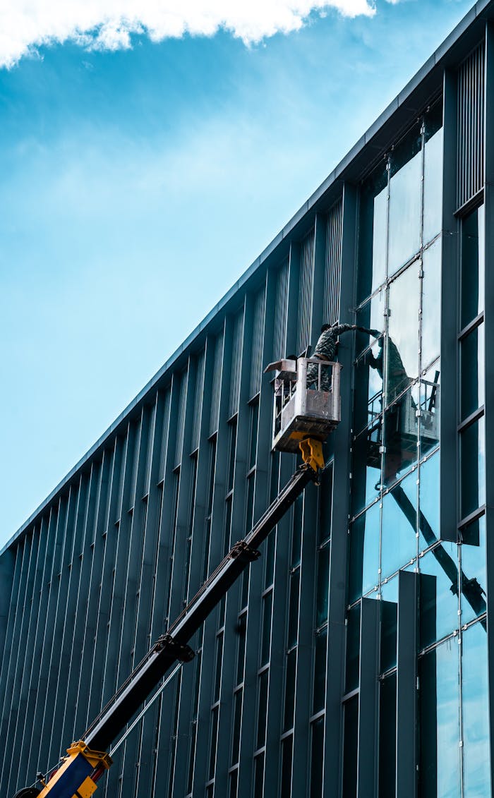 gallery-2 Person on crane cleaning skyscraper windows under blue sky.