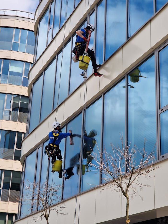 services-03 Two window cleaners using ropes on a modern skyscraper, showcasing urban professional maintenance.