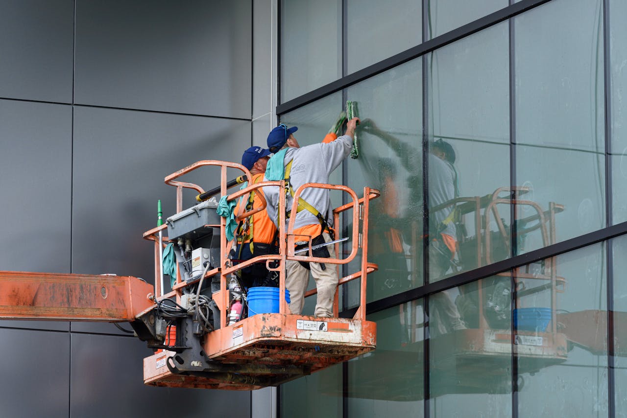 about-img Window cleaners working on a skyscraper using a hydraulic lift in urban setting.