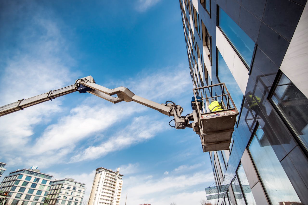 services-img Construction worker on a lift near high-rise building against blue sky.